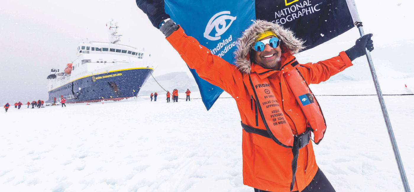 Image: A man holds a Lindblad Expeditions-National Geographic flag in Antarctica. (Photo Credit: Lindblad Expeditions-National Geographic)