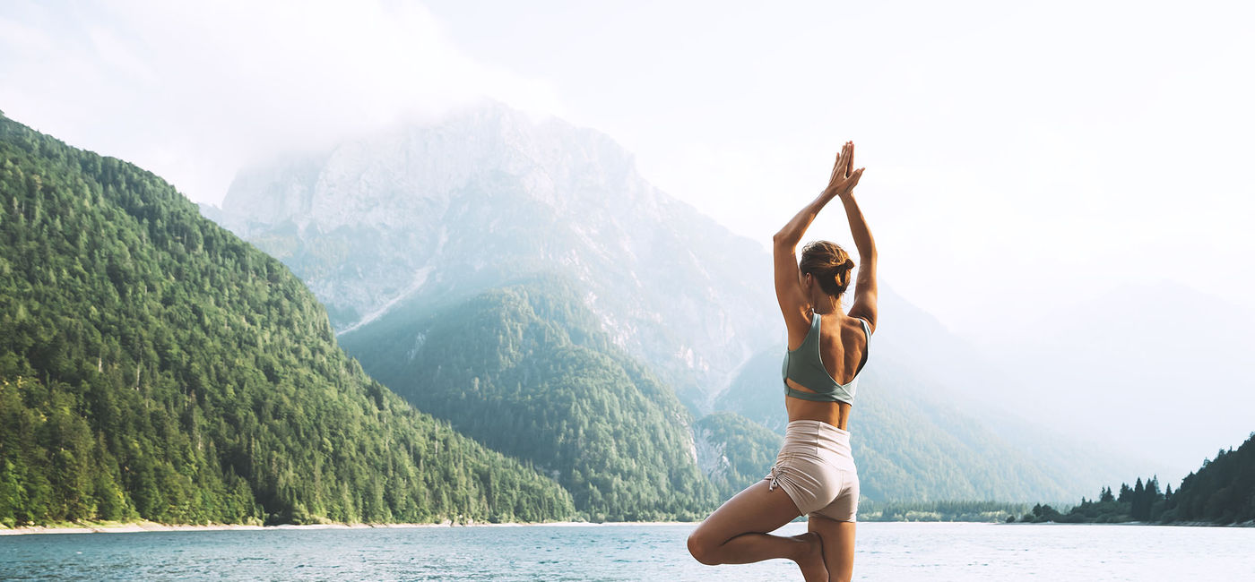 Image: A traveler doing a yoga pose near the water. (photo via Wellness Travel University)