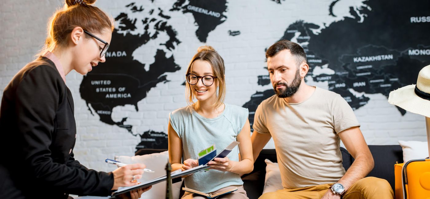 Image: Young couple at a travel agency office. (photo via RossHelen/iStock/Getty Images Plus)